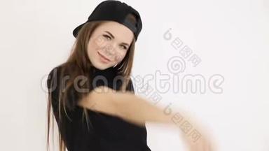 一个穿着黑色<strong>嘻哈</strong>服装，戴着<strong>帽子</strong>的十几岁女孩在白色的墙壁上跳舞-特写、手持射击、小深度。